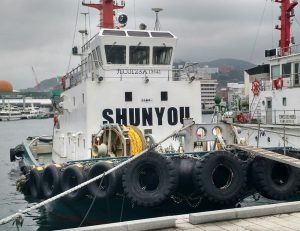 Tug boat with its name "SHUNYOU" painted in large capitals on the front of the superstructure.