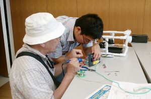 Japanese teacher helping Japanese school student with soldering.