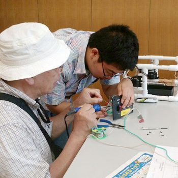 Japanese teacher helping Japanese school student with soldering.