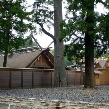 A new-looking timber building behind a fence in woodland, built in the style of a pre-buddhist Shinto shrine