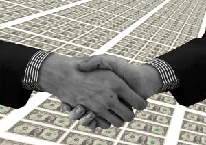 Two men in suits shaking hands across a large amount of money