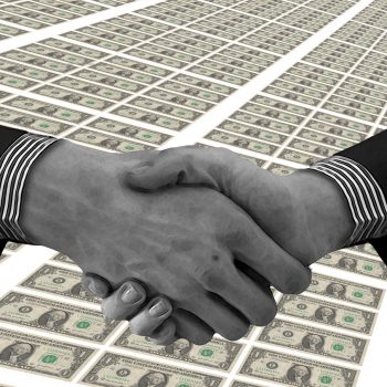 Two men in suits shaking hands across a large amount of money