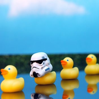 A row of yellow plastic ducks, where the second one is wearing a stormtrooper helmet from Star Wars