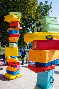 Photograph of an art installation consisting of two very high piles of brightly coloured luggage.