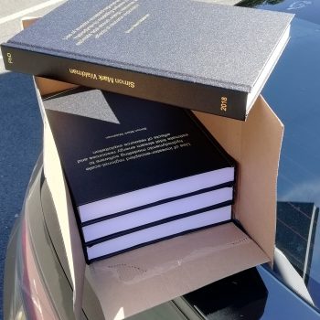 Four copies of a hard-bound thesis, posed in a box in the sun.